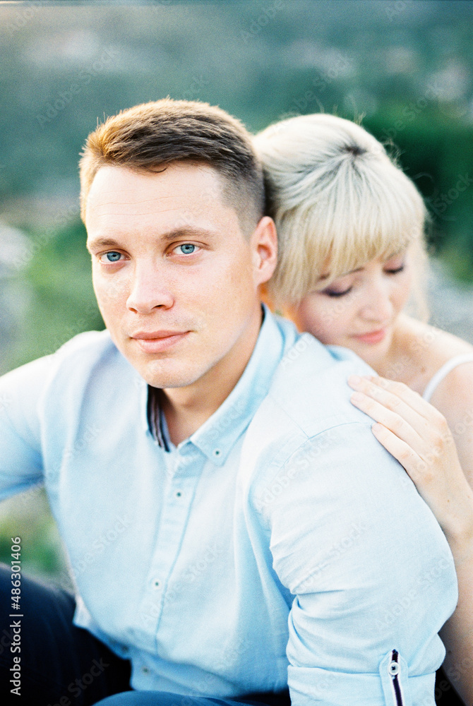 Woman hugs man from behind, resting her head on his shoulder. Portrait