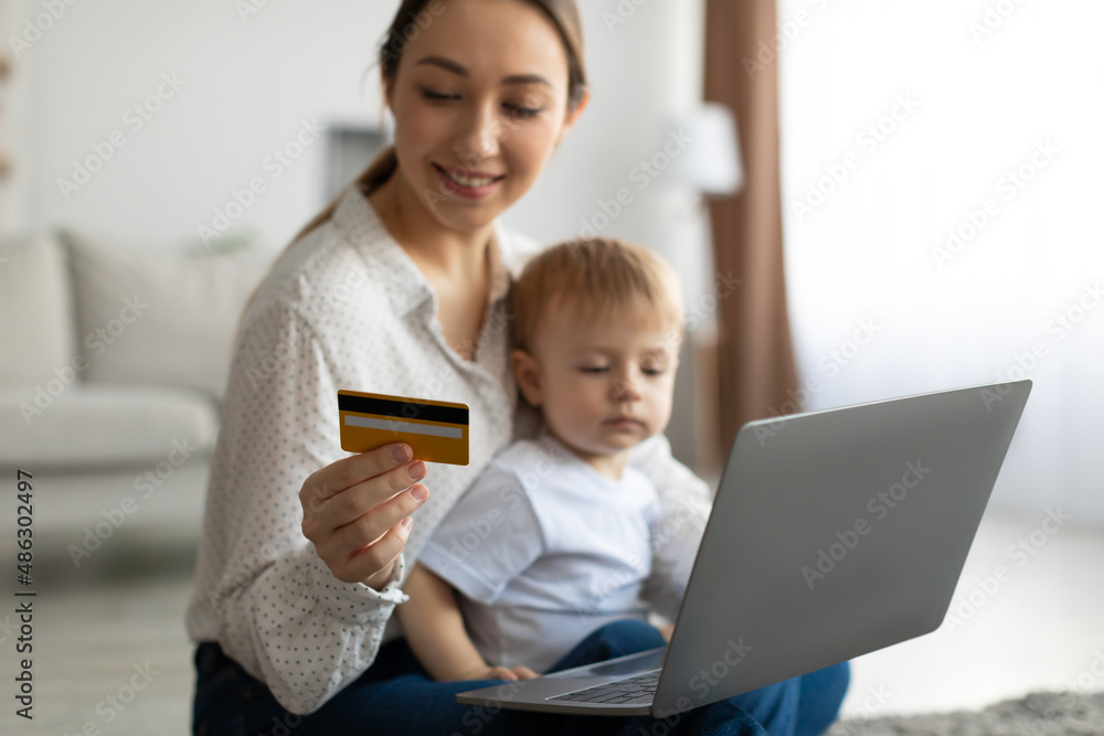 Happy mother and her little son shopping online with laptop computer and credit card, sitting together in living room Happy mother and her little son shopping online with laptop computer and credit card, sitting together in living room