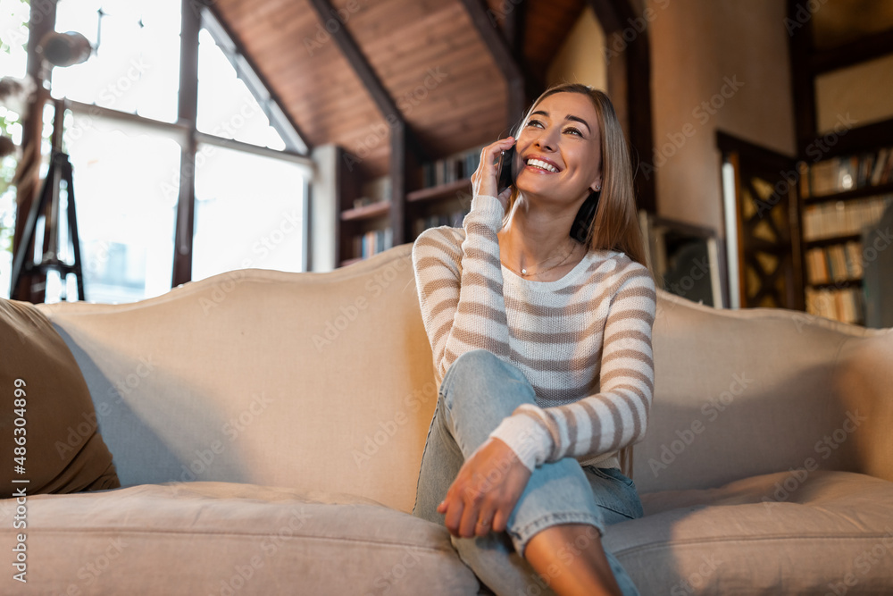 Obraz premium Cheerful woman talking on cellphone sitting on couch