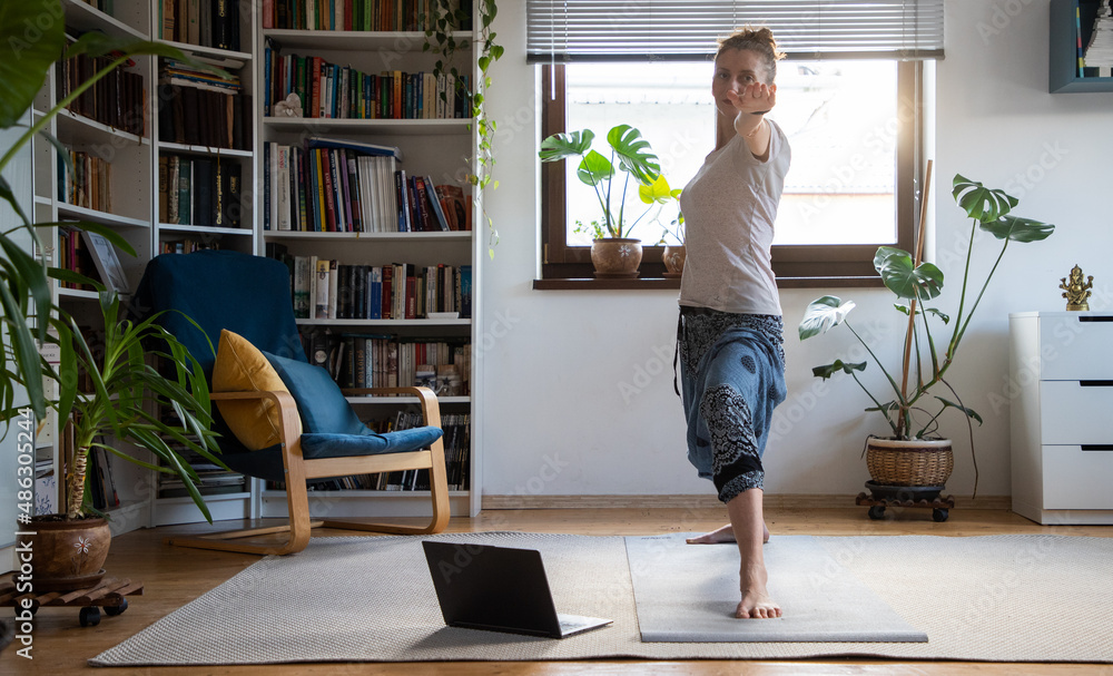 wwoman doing yoga at home online with laptop - warrior 2 pose, Virabhadrasana 2 wwoman doing yoga at home online with laptop - warrior 2 pose, Virabhadrasana 2