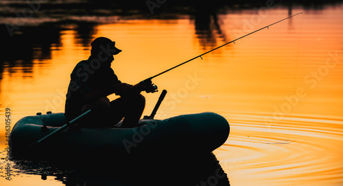 fisherman silhouette in a boat fishing on a lake at sunset