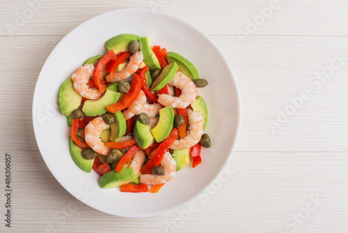 Top view on a plate of salad with avocado, pepper, shrimps, capers on white plate. Mediterranean cuisine.
