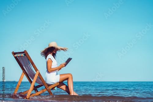 Photo Side view of woman in sunhat who using laptop while lying on the beach chaise lo