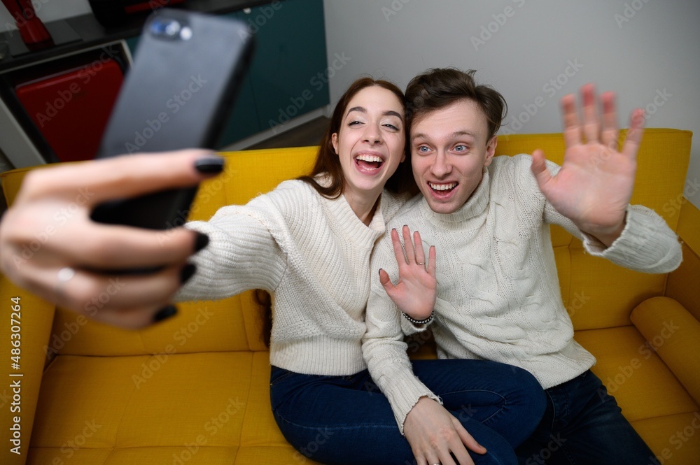 Fototapeta premium a young married couple at home. They sit on the couch and take selfies or talk on video communication
