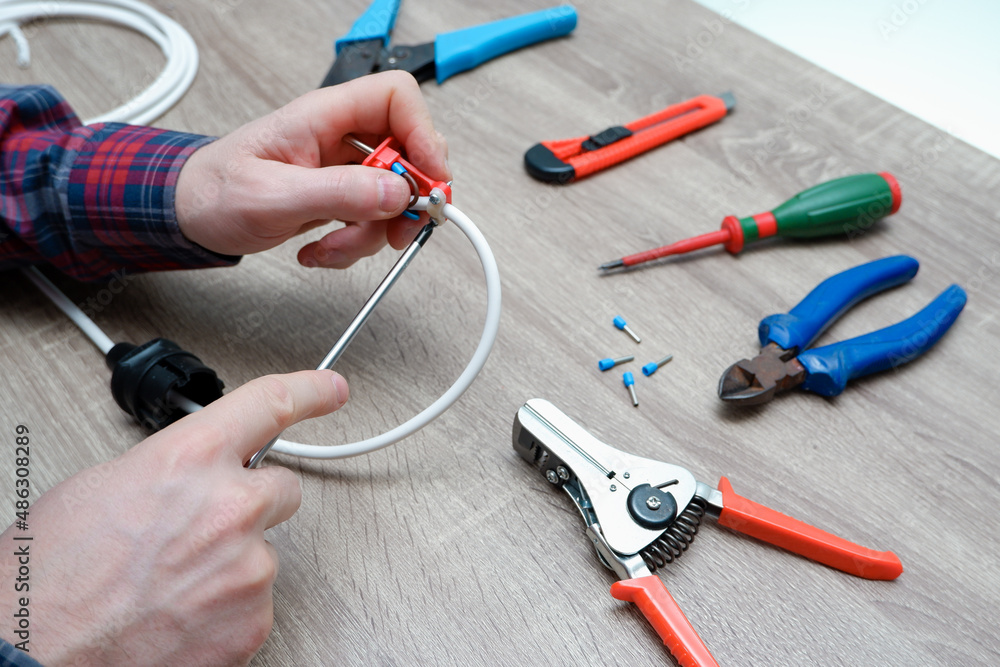 A male electrician changes the plug on an electric wire. Working with electrical tools. Stripper, crimp, screwdriver, wire cutters. Electrician connecting wires A male electrician changes the plug on an electric wire. Working with electrical tools. Stripper, crimp, screwdriver, wire cutters. Electrician connecting wires