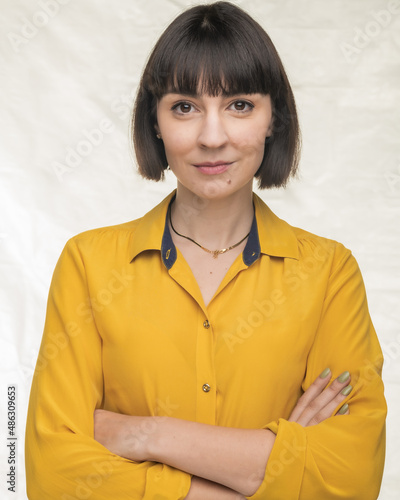 American woman with short brown hair poses in studio in a yellow shirt.