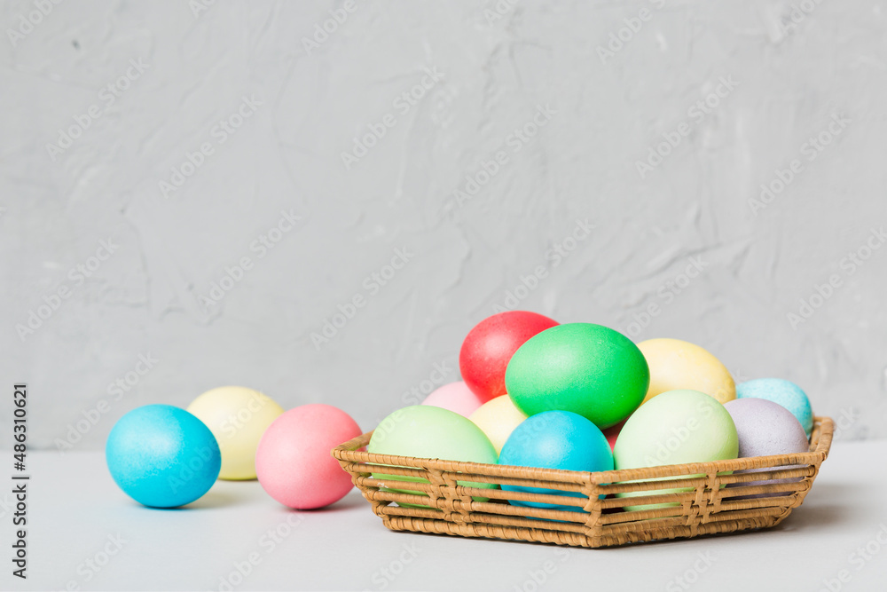 Naklejka premium Multi colors Easter eggs in the woven basket on colored background . Pastel color Easter eggs. holiday concept with copy space