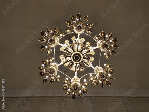 Luxurious interior chandelier has lit candles and a dark background. Noble candelabra hang from the ceiling