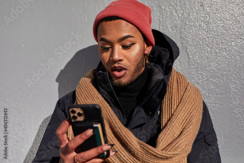 Photography USA, New York City, Queer man in warm clothing looking at smart phone