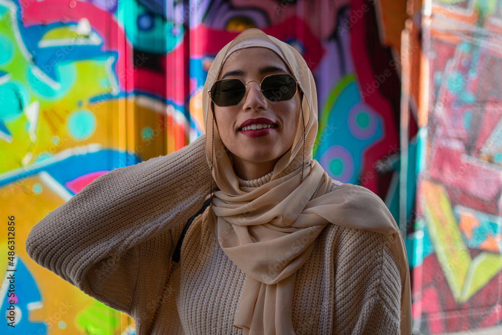 Portrait of young muslim woman wearing hijab head scarf in city while looking at camera. Closeup face of cheerful woman covered with headscarf smiling outdoor sunglasses. Islamic girl outdoors Portrait of young muslim woman wearing hijab head scarf in city while looking at camera. Closeup face of cheerful woman covered with headscarf smiling outdoor sunglasses. Islamic girl outdoors