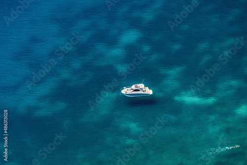 Leisure boat panoramic with swimmer on a turquoise calm sea. Elevated view of anchored small cruiser with a person on crystal clear waters. © bestravelvideo