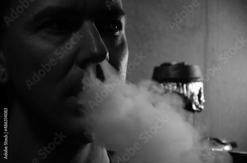 Caucasian man smokes hookah. Portrait of young man smoking shisha pipe and exhaling smoke. The concept of relax. photo