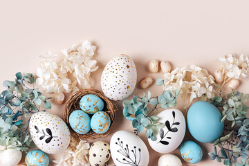 Easter eggs with sweets and flowers on beige. Happy Easter concept. White and blue eggs and cute nest with candy