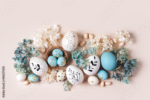 Easter eggs with sweets and flowers on beige. Happy Easter concept. White and blue eggs and cute nest with candy