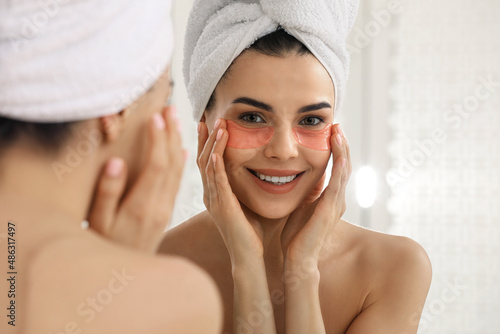 Beautiful young woman with under eye patches near mirror at home