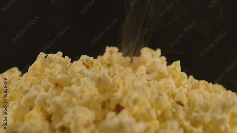 Pile of appetizing popcorn with dissipating steam. Woman's hand takes freshly cooked hot popcorn. Close up. Unrecognizable person eating crunchy appetizer. Concept of snack for movie. Pile of appetizing popcorn with dissipating steam. Woman's hand takes freshly cooked hot popcorn. Close up. Unrecognizable person eating crunchy appetizer. Concept of snack for movie.