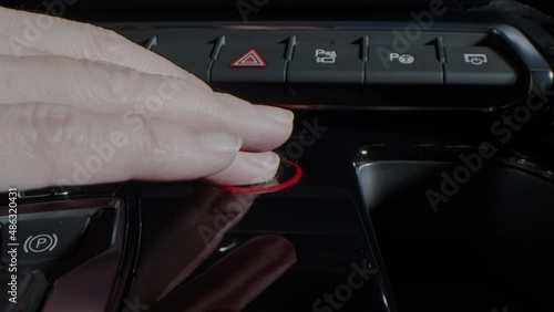 a woman's hand starts an electric car by placing her finger on the start button in her electric car. luxury car interior. Close-up. Side view
 photo