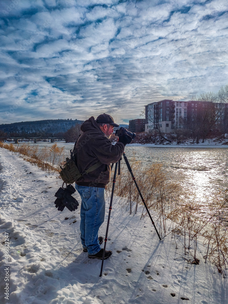 A male photographer with his camera and tripod takes photos while walking the Chenango River Walk in Binghamton in Upstate NY.  