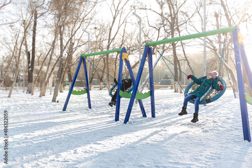 children boy and girl ride on a swing in the park in winter. winter walk in the park.lifestyle, winter clothes 
