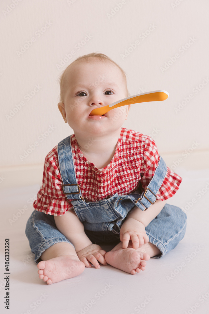 Portrait of cute baby with a spoon in overall jeans and a red plaid shirt. Portrait of cute baby with a spoon in overall jeans and a red plaid shirt.