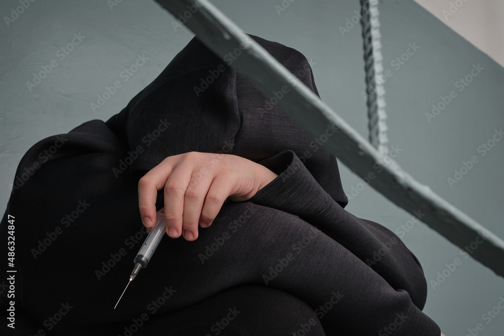 Depressed teenage sitting alone after using drugs over grunge concrete