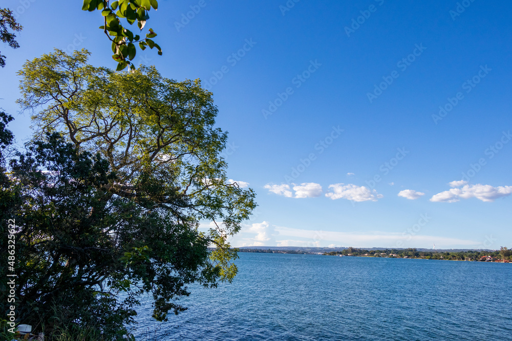Lago de águas calmas com uma árvore a esquerda sob um céu azul. Lago de águas calmas com uma árvore a esquerda sob um céu azul.