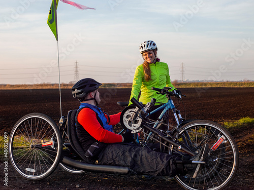 Obraz na płótnie Disabled man on handcycle and woman with bicycle in rural landscape