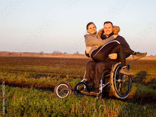 Smiling man on wheelchair in field carrying woman