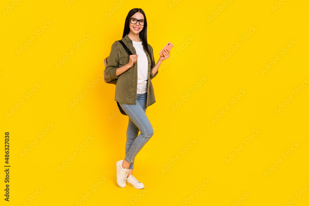 Full size photo of nice young lady hold telephone wear bag spectacles shirt jeans shoes isolated on yellow background