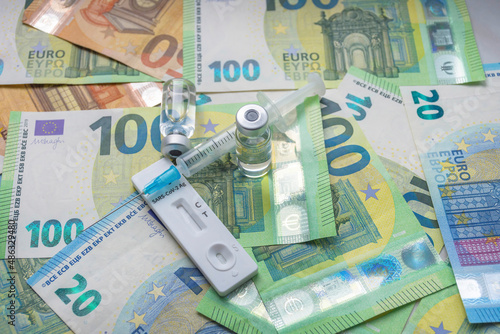Money (Euro currency banknotes) with medical mask, antigen test, vaccine bottles and syringe. Financial crisis due to Coronavirus losses, selective focus