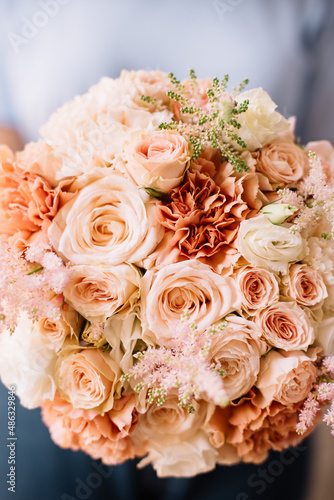 Very nice young woman holding big and beautiful round wedding bouquet of fresh Astilbe, roses, carnations, matthiola in colors, cropped photo, bouquet close up on the wooden background