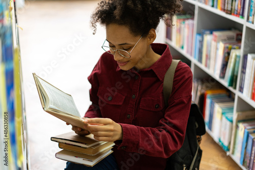 High angle view of the multiracial student girl choosing books at the library. Woman preparing to the exams concept