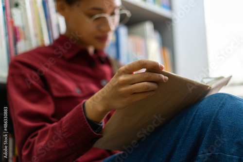 Portrait view of a very busy young brunette multiracial student sitting at the floor and reading something at the book