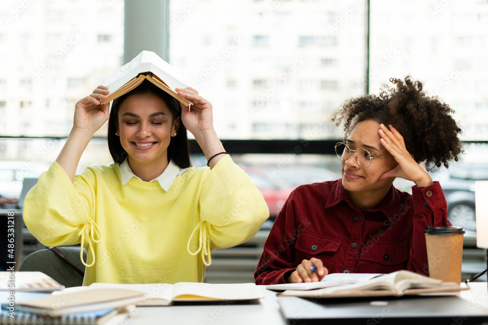 Two young women having fun and working together with happiness while sitting at table. Young university student studying together Two young women having fun and working together with happiness while sitting at table. Young university student studying together