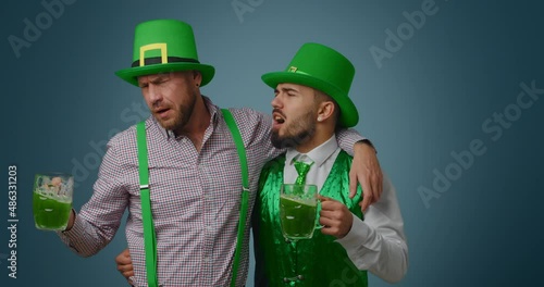 Drunk bearded men singing and drinking green beer on color background. St. Patrick Day celebration