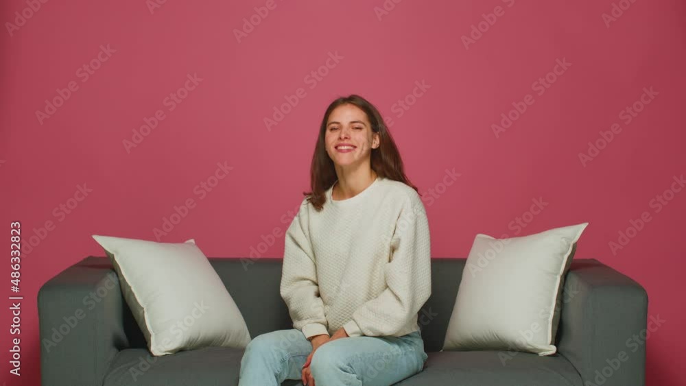Smiling young girl winking, nodding head yes, flirting, hinting, sitting on sofa, express optimism, positive emotion Smiling young girl winking, nodding head yes, flirting, hinting, sitting on sofa, express optimism, positive emotion