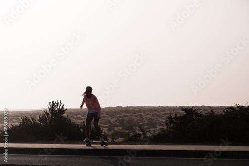 Skater woman silhouette riding on a road by a desertic landscape in Fuerteventura island photo