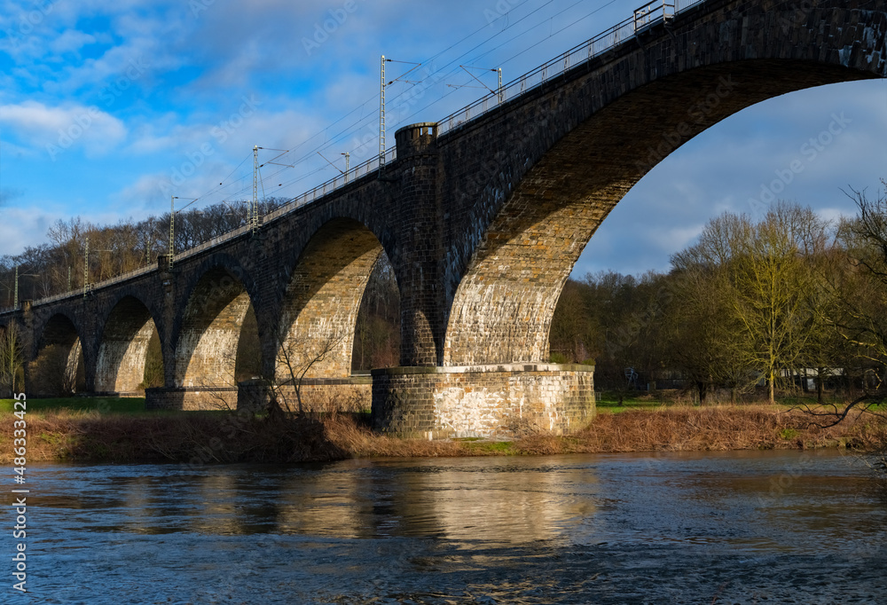 Railway Viaduct over Ruhr river in Witten Germany. Historic brick stone construction with big arches in a curve of main line from Hagen to Dortmund seen from below with wide angle and warm light.