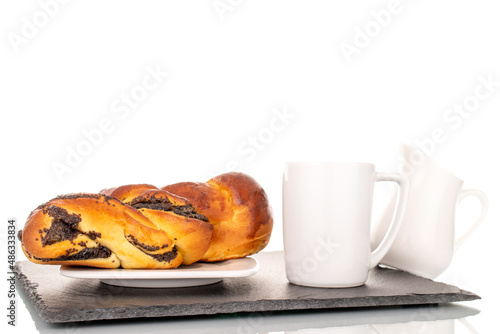 One flavorful homemade poppy seed bun with ceramic saucer, milk jug and cup on a slate stone, macro, isolated on a white background.

