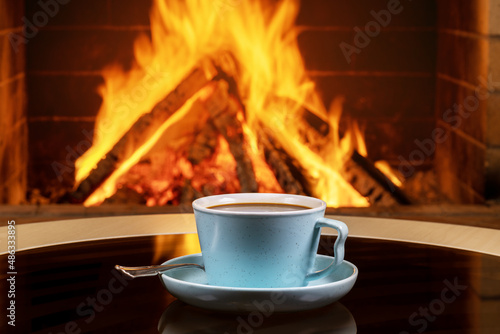 A cup of tea or coffee and old books on a background of burning fireplace.