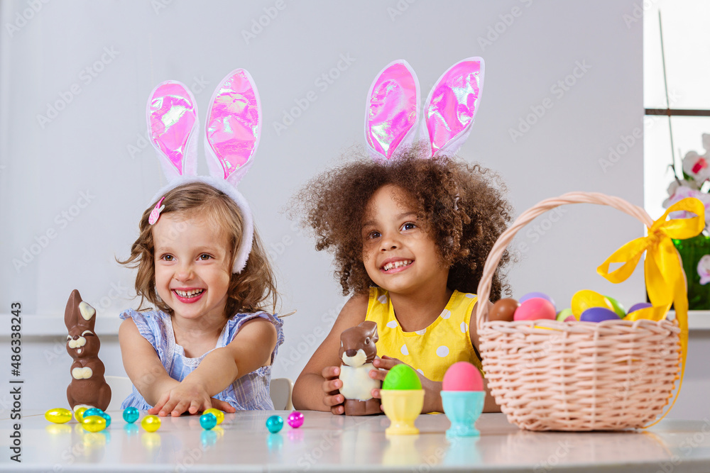 Black and White girl in pink bunny ears play with Easter chocolate bunny