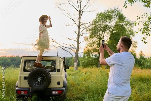 Summer vacation together, traveling by car, man photographing woman on smartphone