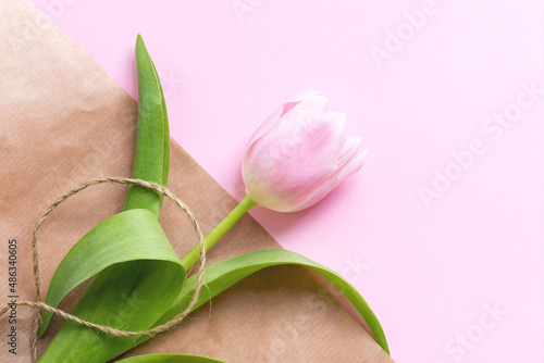 Beautiful delicate pink tulip flower and waxed cord on packaging craft paper background
