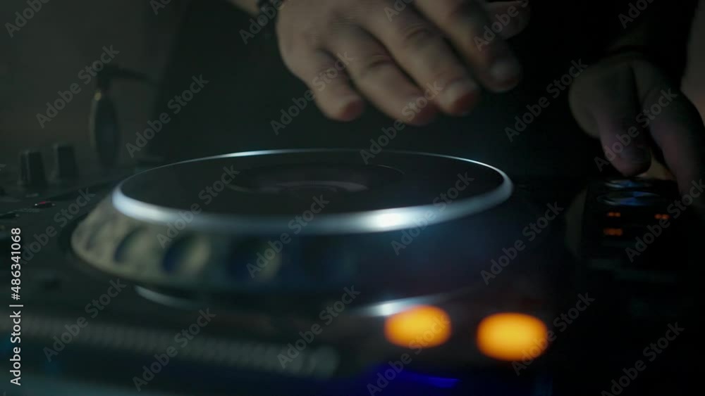 Hands of unknown DJ touching vinyl plate, mixing and scratching music using mixer controller, rocking party in nightclub. Close up, slow motion Hands of unknown DJ touching vinyl plate, mixing and scratching music using mixer controller, rocking party in nightclub. Close up, slow motion
