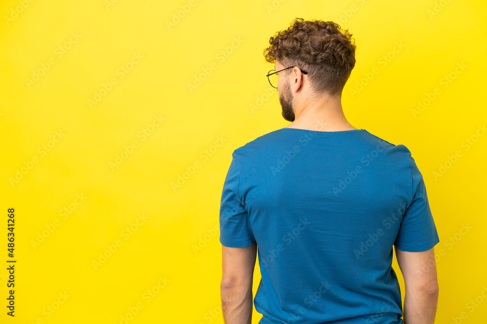Young handsome caucasian man isolated on yellow background in back position and looking side Young handsome caucasian man isolated on yellow background in back position and looking side