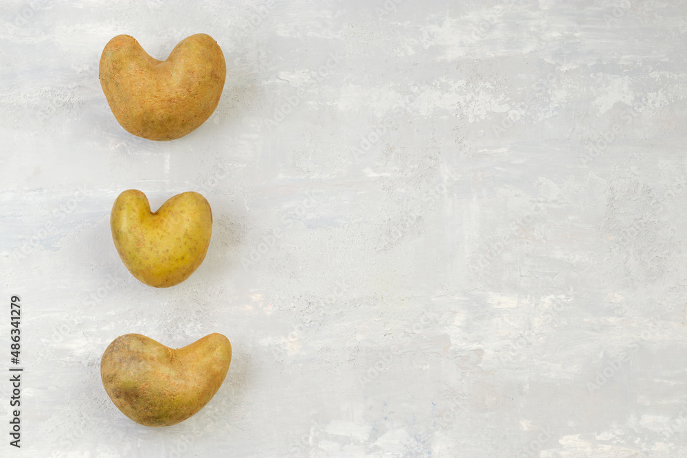 Obraz premium Some ugly heart-shaped potatoes on a gray background. Funny concept of vegetables or food waste. Top view. Copy space.