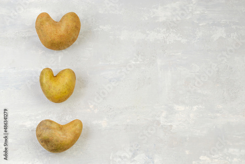 Some ugly heart-shaped potatoes on a gray background. Funny concept of vegetables or food waste. Top view. Copy space.