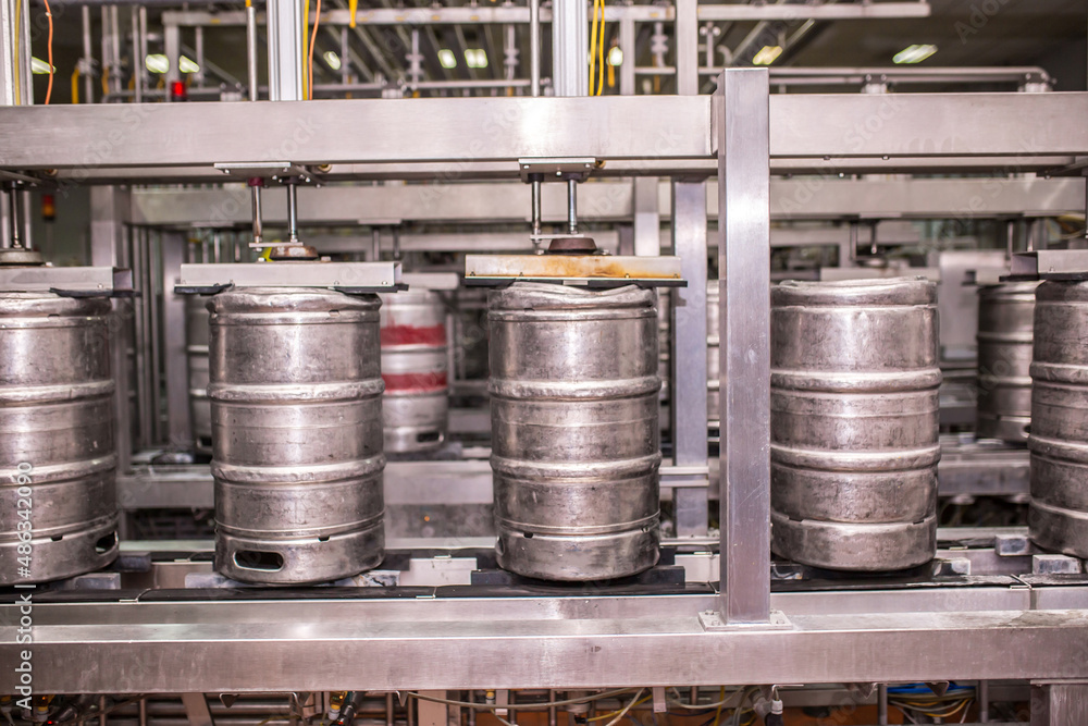 Brewery, bottling beer on aluminum kegs on conveyor lines. Industrial work, automated modern food and beverage production. Brewery, bottling beer on aluminum kegs on conveyor lines. Industrial work, automated modern food and beverage production.