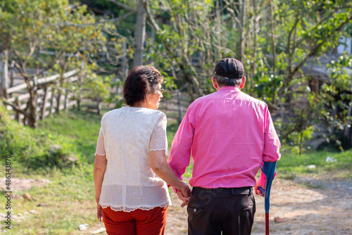 Beautiful unknown elderly couple seen from the back walking through the countryside while using cane. © Anderson Piza