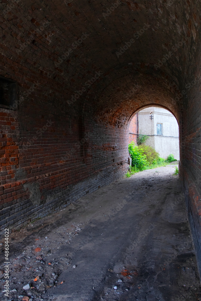 The tunnel of the gateway of the old red brick house. A tunnel with an arched vault. The old courtyard can be seen in the distance. Summer. Daylight.